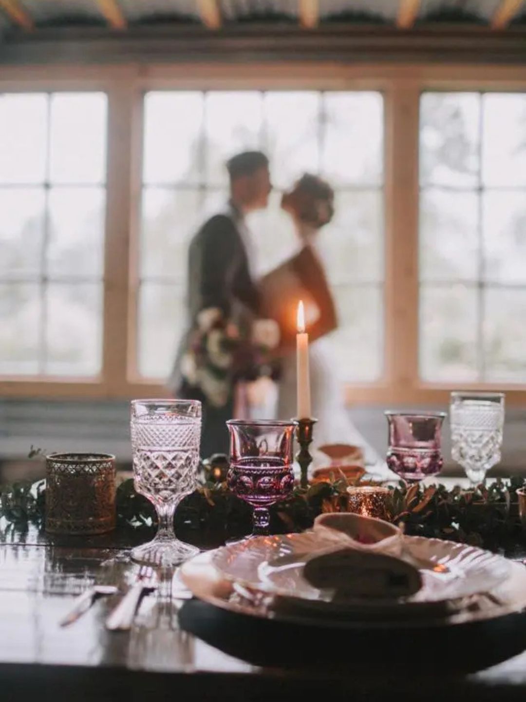 Closeup of wedding head table with blurred silhouette of bride and groom in front of the reception venue windows