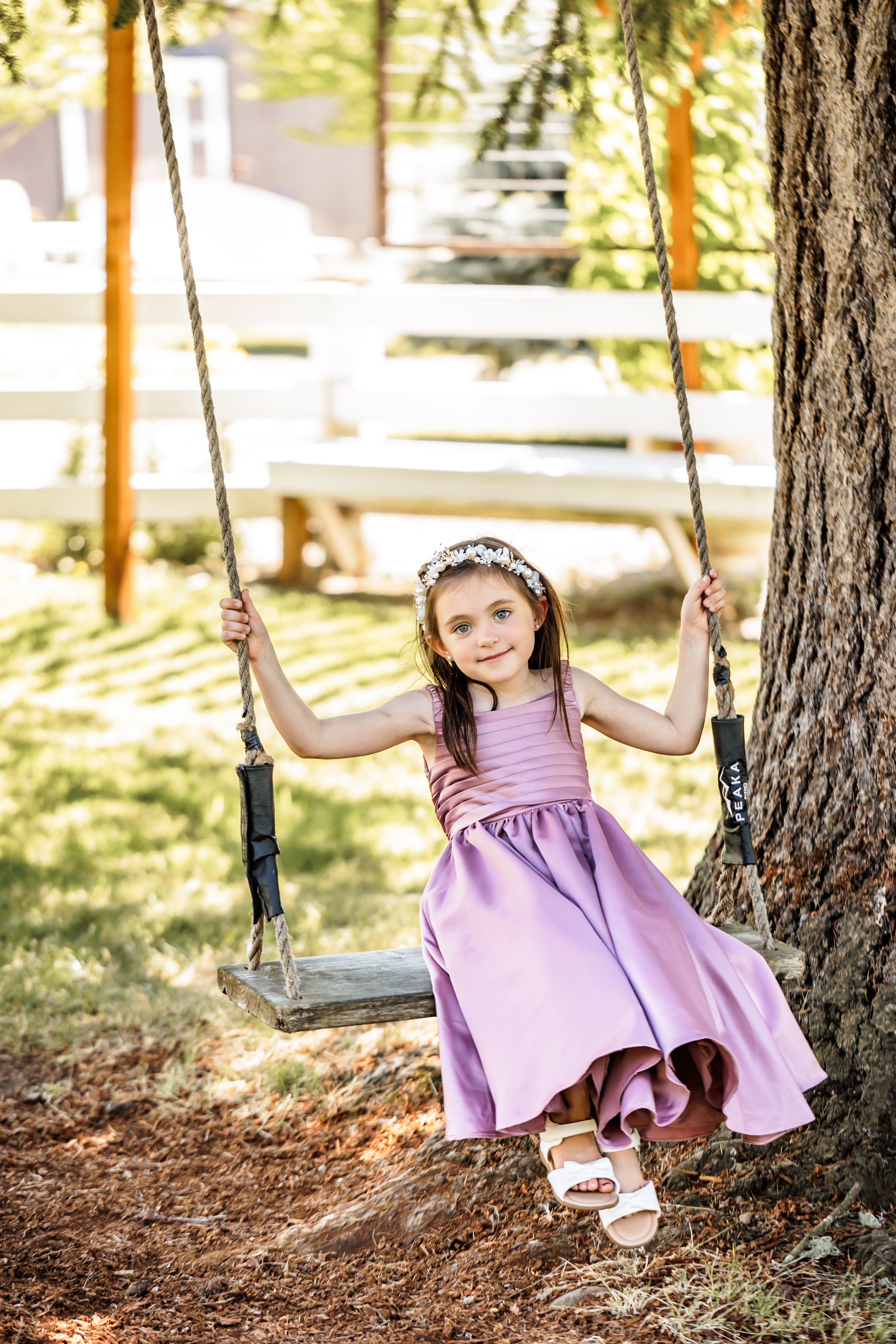 Flower girl in muave dress smiling while sitting on a wooden tree swing