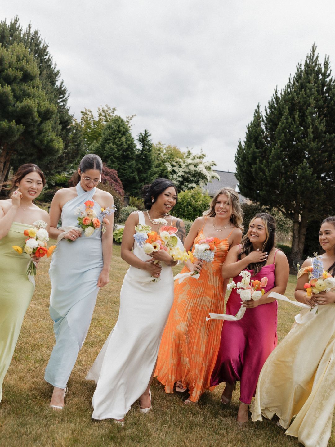 Bride in modern white gown walking with five bridesmaids each in a different bright citrus colored dress holding vibrant citrus inspired flower bouquets