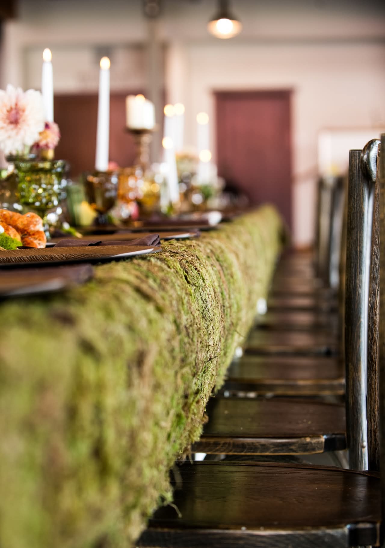 Closeup of table scape featuring a live moss tablecloth, wooden charger plates, goblets in autumn hues and flickering candlelight 