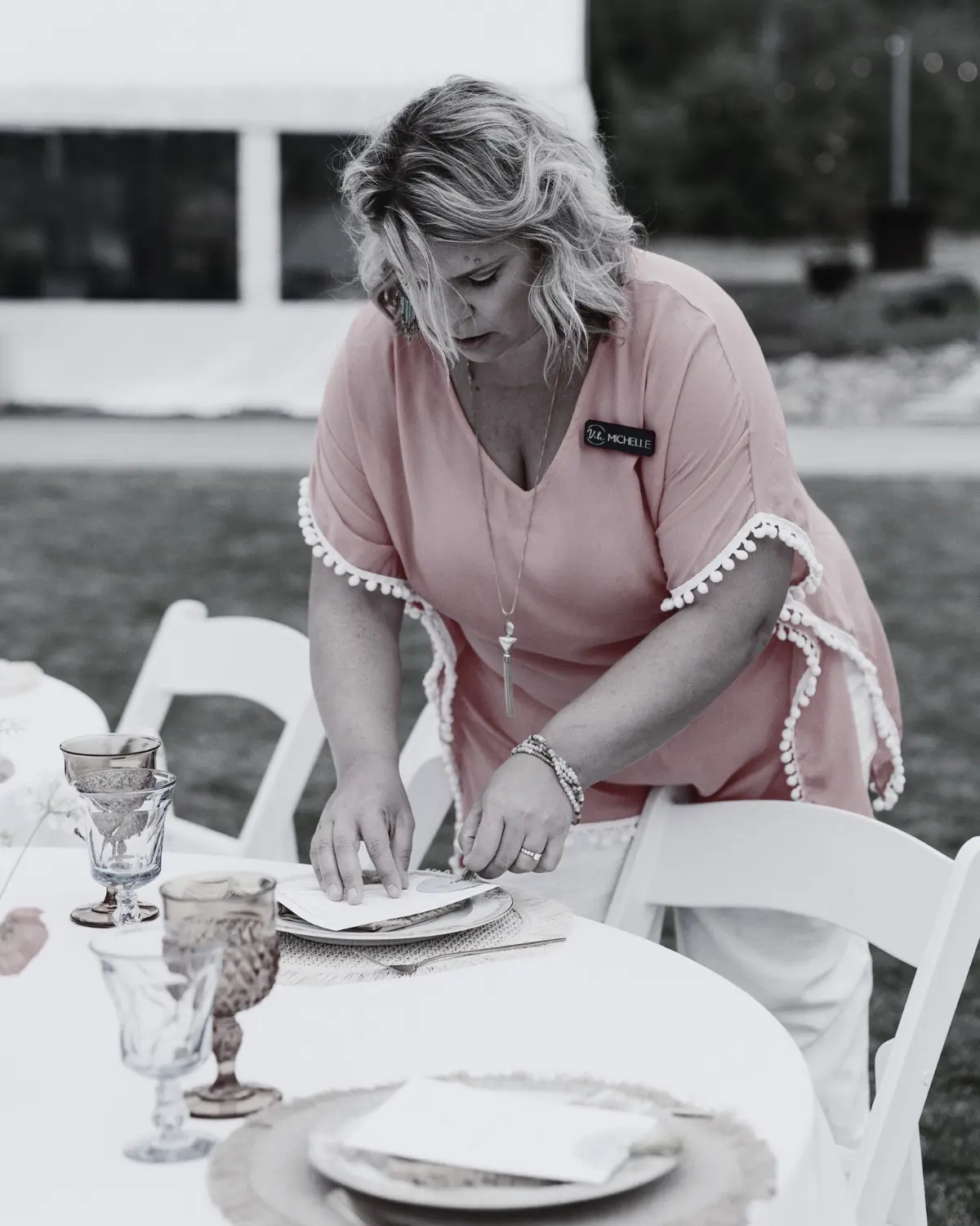 Event coordinator setting glassware and tableware on an outdoor wedding reception table