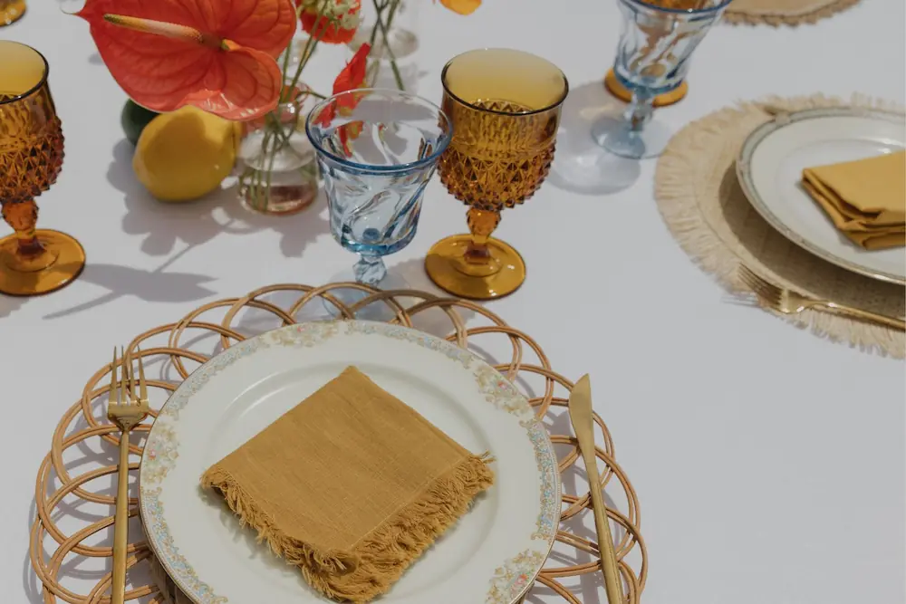 Citrus-themed table setting with a woven placemat, amber goblets, golden napkin, and vibrant orange floral centerpiece
