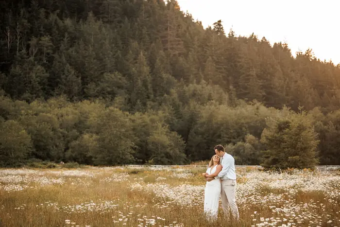 Bride and groom in a field of white wild flowers with green forest in the background