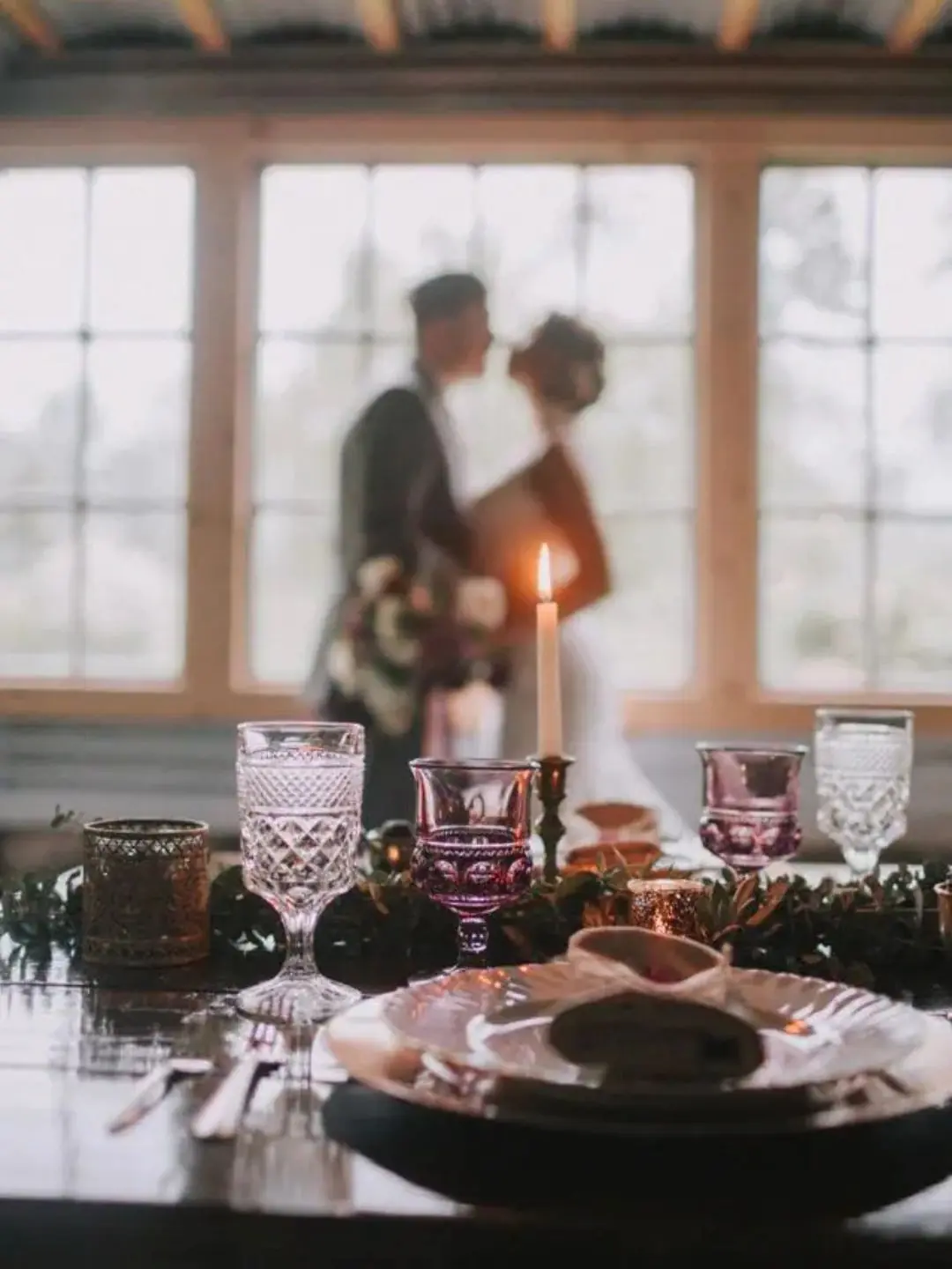 Closeup of wedding head table with blurred silhouette of bride and groom in front of the reception venue windows