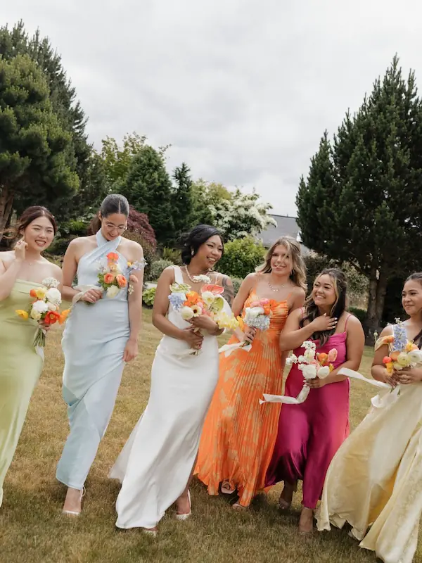 Bride in modern white gown walking with five bridesmaids each in a different bright citrus colored dress holding vibrant citrus inspired flower bouquets