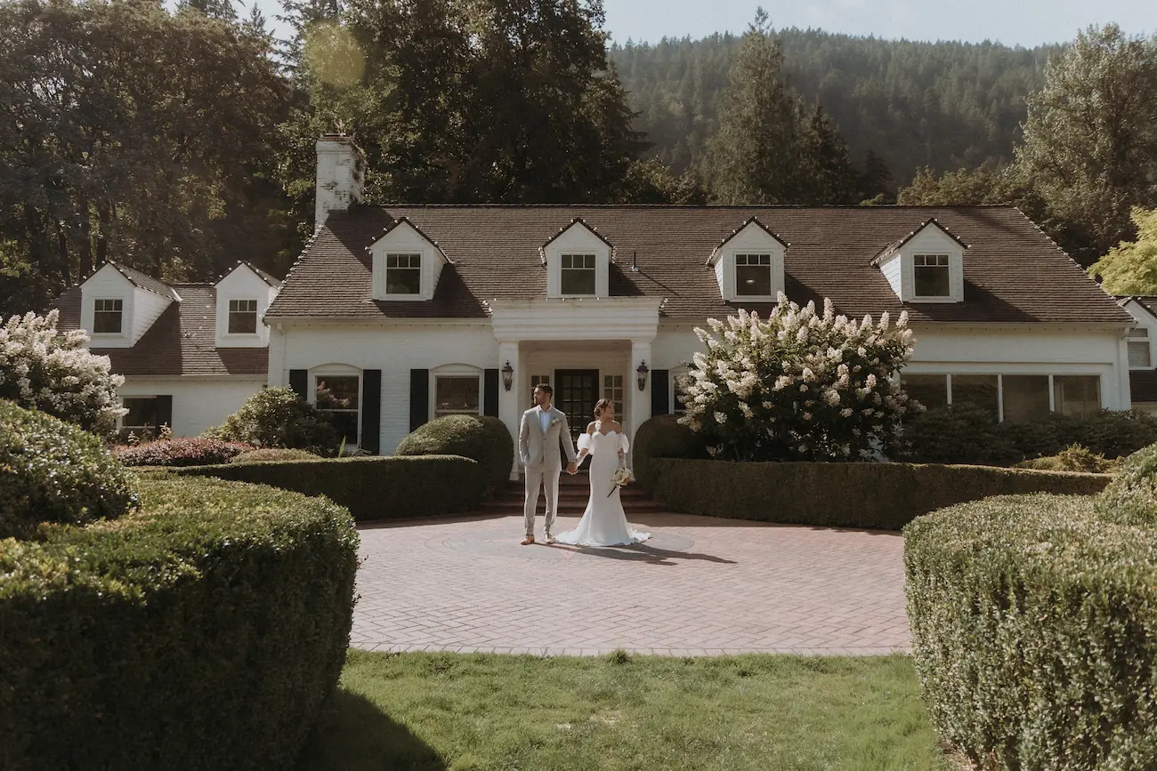 Bride and groom standing on a stone pathway in front of a historic white estate