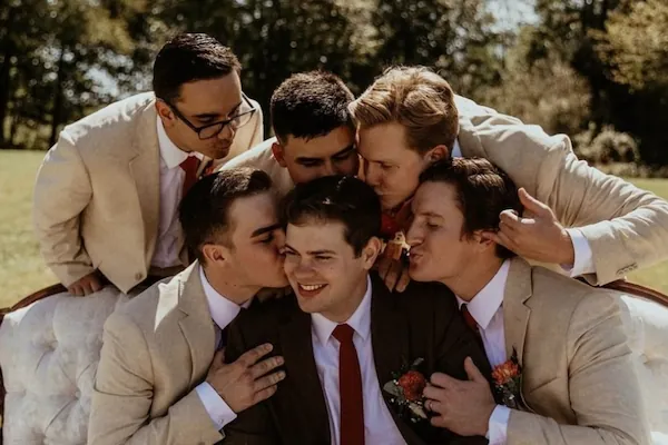 Groomsmen playfully hugging the groom outdoors