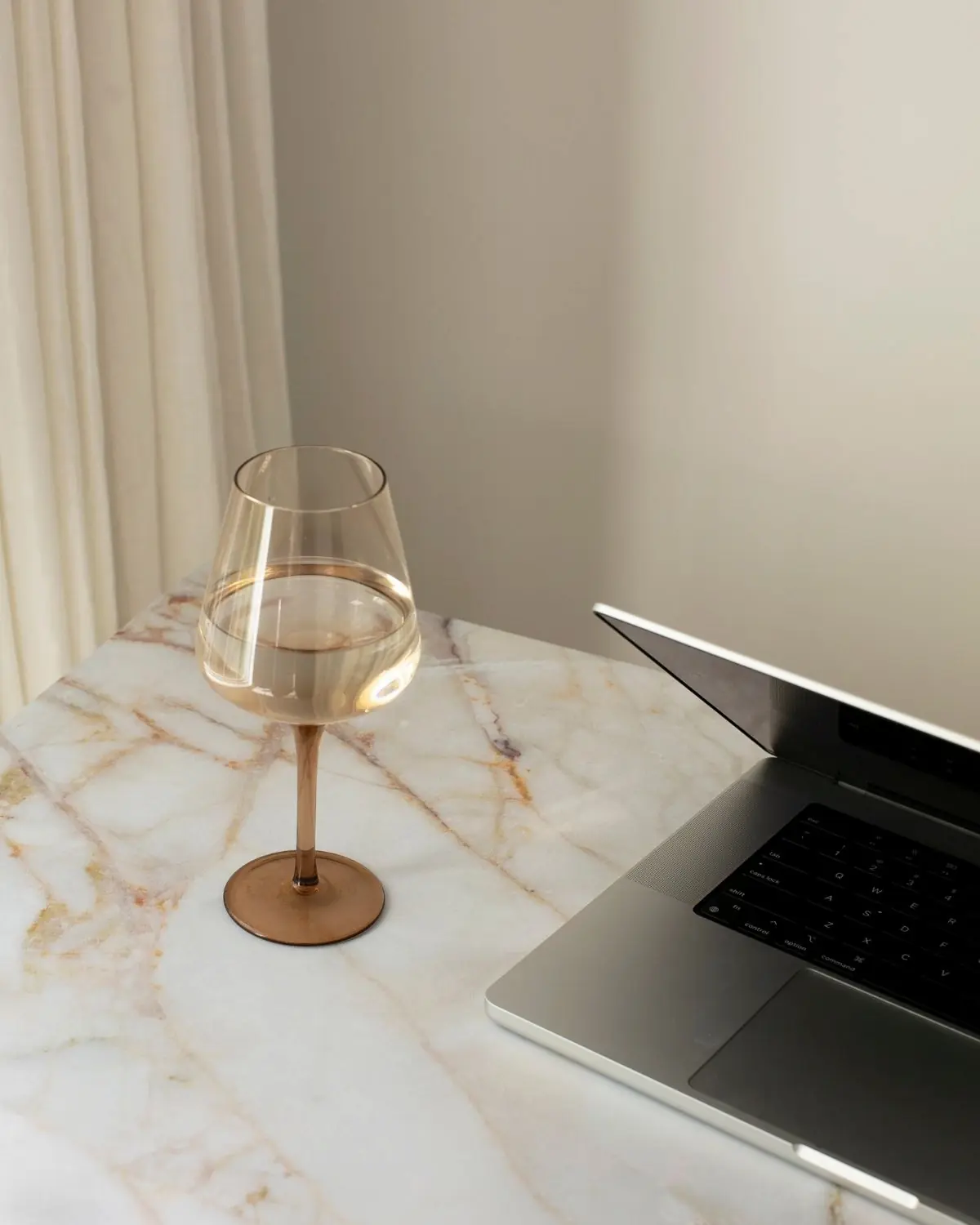 Modern event planning workspace featuring an open laptop, a glass of wine, and soft natural light by a window