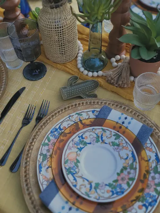 Southwest place setting featuring a blue-patterned plate, woven placemat, blue glassware, and greenery centerpieces