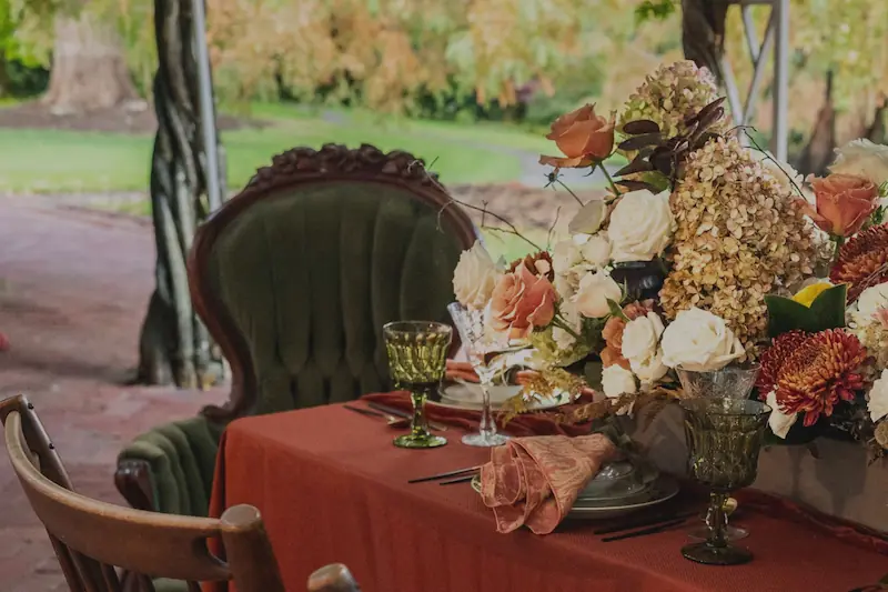 Outdoor garden lounge vignette featuring a green velvet armchair, small accent table, and earthy floral arrangement